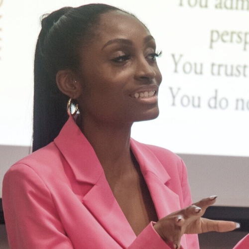 Monaye giving a lecture in a pink blazer